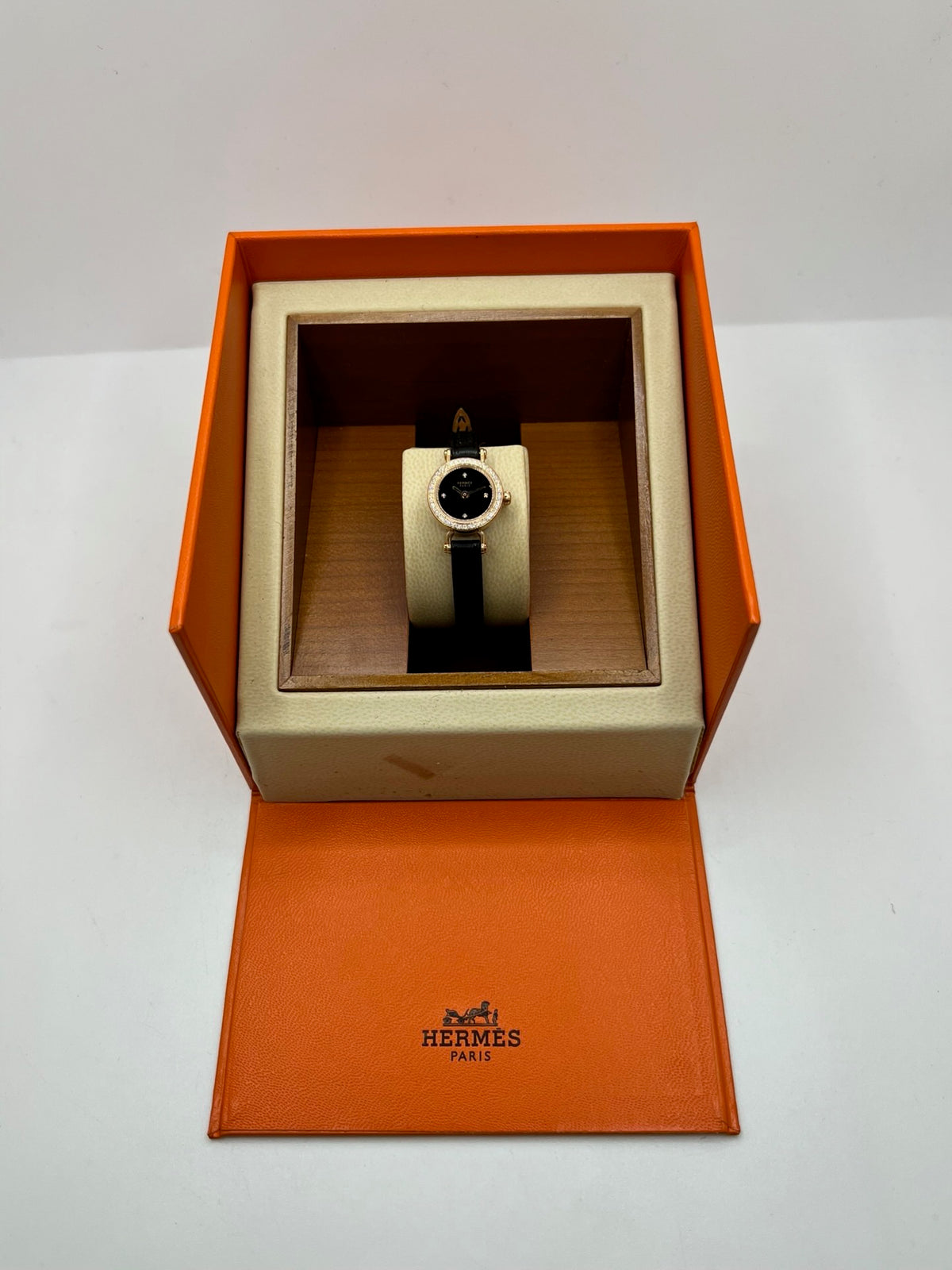 Montre Hermès Faubourg FG4.171 pour femme, dotée d’un élégant boîtier en or rose de 15,5 mm et d’un mouvement quartz. Elle se distingue par son cadran noir sans chiffres, protégé par un verre saphir, et son bracelet en cuir noir avec boucle ardillon en or rose. Cette montre de luxe Hermès associe raffinement, élégance et discrétion. Modèle d’occasion en très bon état, révisé en interne en octobre 2026 et livré avec son coffret d’origine.