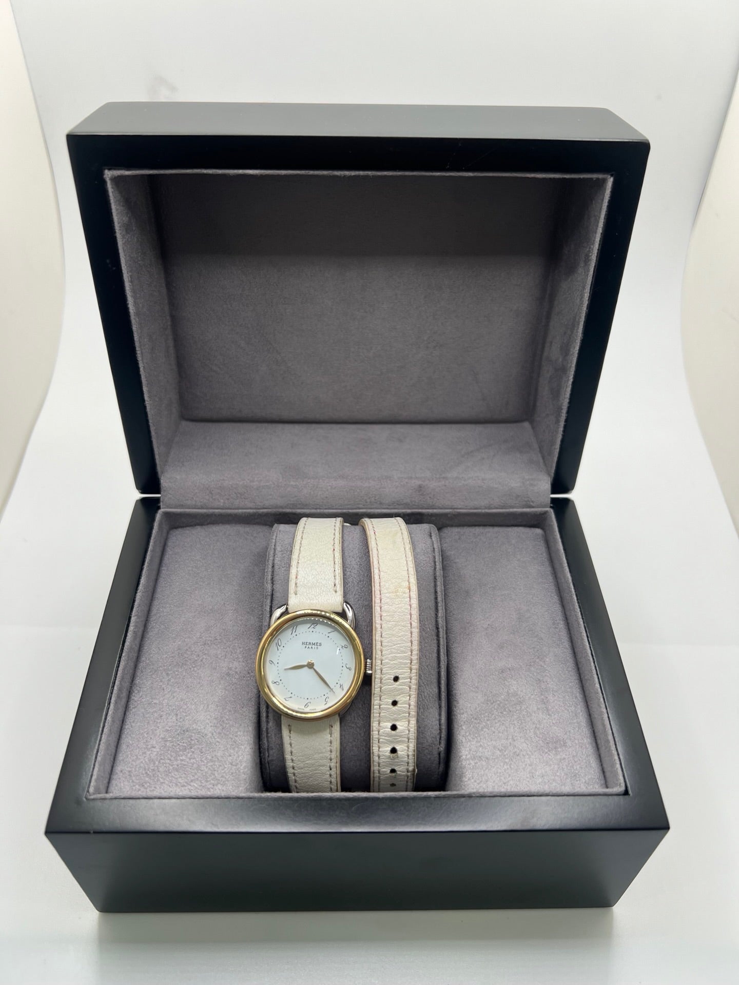 Élégante montre Hermès Arceau pour femme, boîtier en or et acier, cadran blanc aux chiffres arabes et bracelet en cuir beige. Ce garde-temps emblématique allie raffinement et savoir-faire horloger français, offrant un design intemporel et une précision quartz idéale pour un style classique et chic.