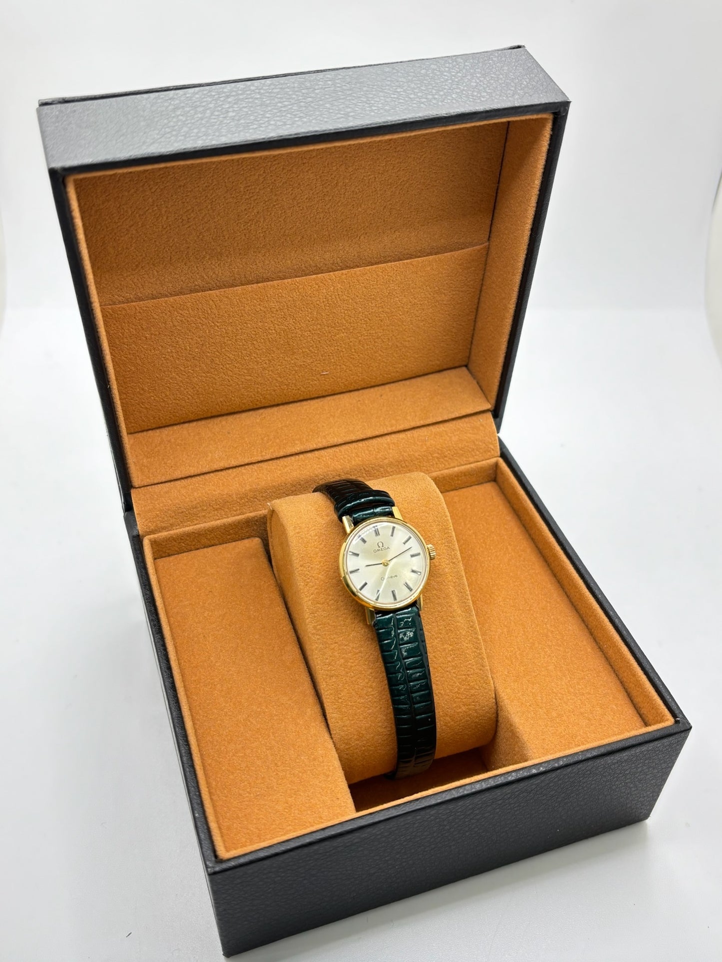 Montre Omega Genève vintage référence 511.0457 pour femme, fabriquée vers 1972 et équipée d'un mouvement à remontage manuel. Son boîtier en acier de 23 mm est associé à un cadran blanc à index bâtons protégé par un verre en matière plastique. Elle est montée sur un bracelet en cuir vert avec boucle ardillon en acier. Révisée en interne et proposée en très bon état, cette montre d'occasion incarne l'élégance discrète et le savoir-faire horloger suisse des années 1970.
