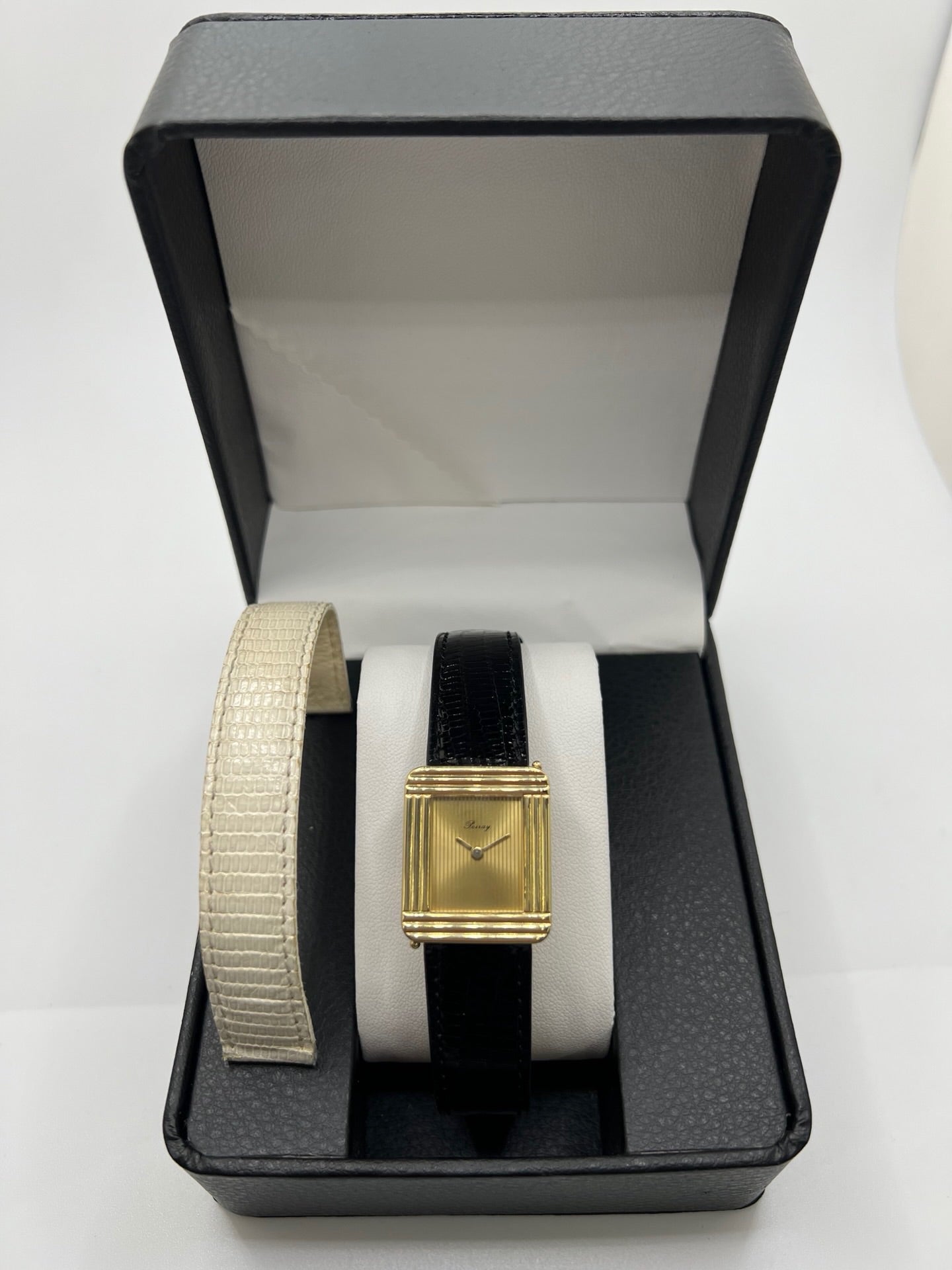 Montre femme Poiray Ma Première en or jaune 18K avec boîtier rectangulaire 22 x 26 mm, cadran doré sans chiffres et verre saphir. Modèle élégant équipé d’un mouvement quartz, bracelet en cuir noir et boucle en acier. Pièce d’occasion en très bon état présentant de légères traces d’usure non perceptibles. Montre raffinée, révisée récemment, idéale pour un style intemporel.