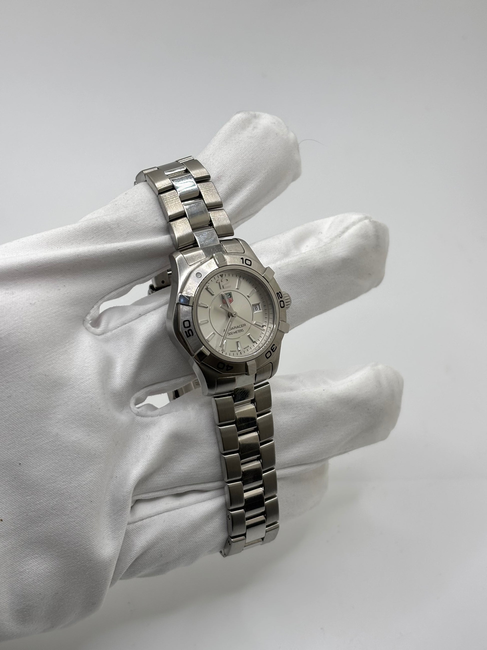 Montre femme TAG Heuer Aquaracer Lady référence WAF1412 en acier avec boîtier 27 mm et bracelet acier. Cadran argent avec chiffres arabes, mouvement quartz précis et étanchéité 30 ATM. Montre de luxe sportive et élégante en très bon état, révisée en 2026, idéale pour un usage quotidien ou une tenue habillée. Détail du boîtier acier poli, montre horlogère suisse féminine, intemporelle et raffinée.