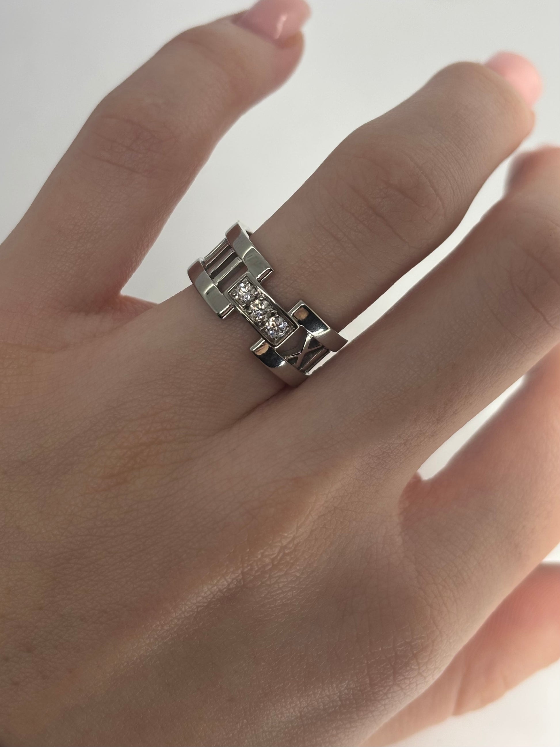 Bague Atlas ring en or blanc signée Tiffany & Co., sertie de diamants totalisant 0,15 carat. Son design graphique emblématique, inspiré des chiffres romains, allie modernité et élégance intemporelle. Un bijou raffiné et lumineux, idéal pour sublimer la main au quotidien ou marquer une occasion spéciale avec une pièce iconique de la joaillerie de luxe.