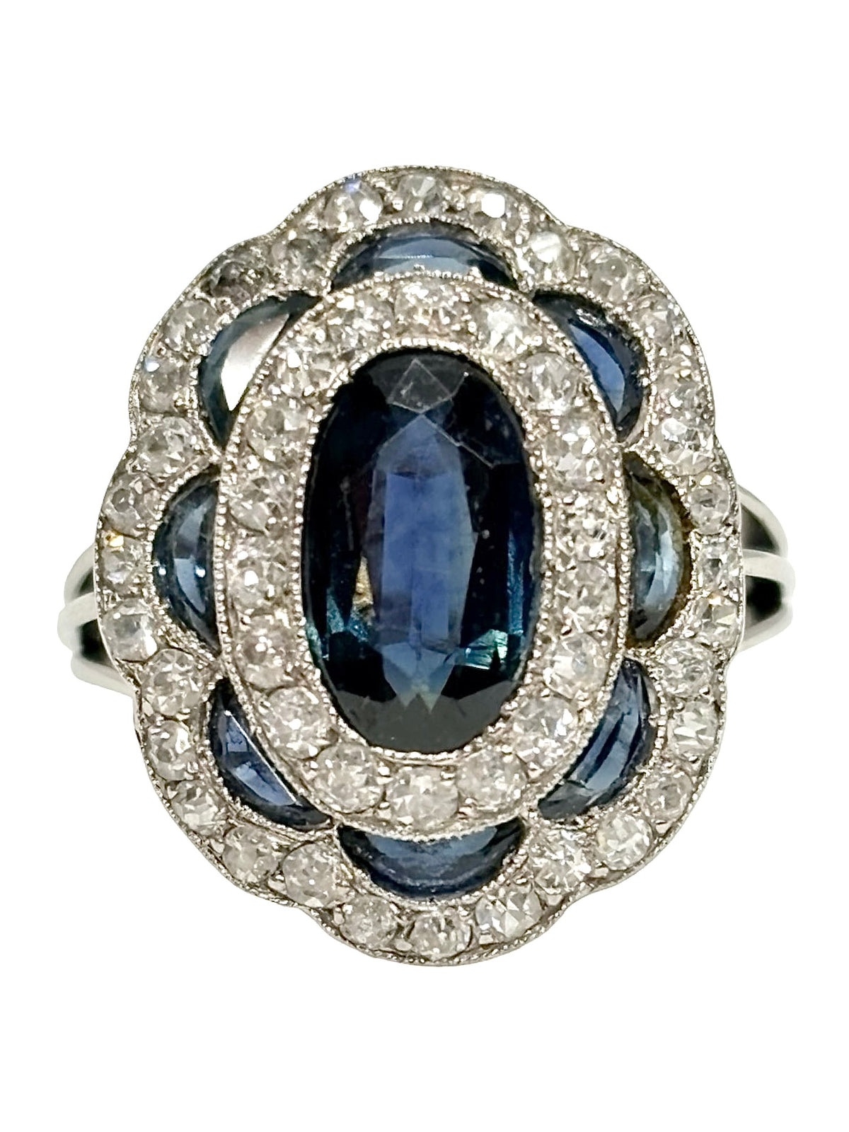 Bague ancienne en or blanc 18K (750 millièmes), sertie d’un saphir naturel central ovale d’environ 2 carats et de petits saphirs naturels en demi-lune. Des diamants naturels de taille ancienne complètent cette pièce de joaillerie pour un poids total d’environ 0,25 carat. Cette bague vintage en or blanc séduit par son élégance intemporelle, ses pierres précieuses et son charme raffiné.