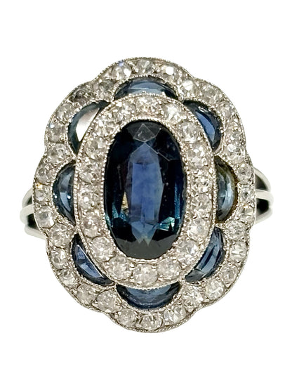 Bague ancienne en or blanc 18K (750 millièmes), sertie d’un saphir naturel central ovale d’environ 2 carats et de petits saphirs naturels en demi-lune. Des diamants naturels de taille ancienne complètent cette pièce de joaillerie pour un poids total d’environ 0,25 carat. Cette bague vintage en or blanc séduit par son élégance intemporelle, ses pierres précieuses et son charme raffiné.