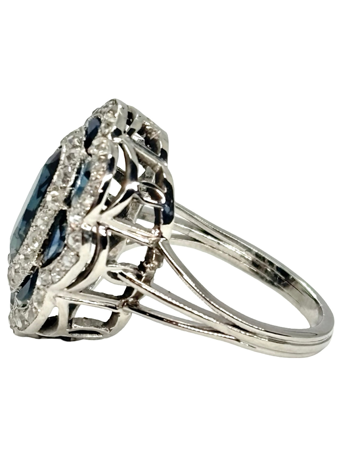Bague ancienne en or blanc 18K (750 millièmes), sertie d’un saphir naturel central ovale d’environ 2 carats et de petits saphirs naturels en demi-lune. Des diamants naturels de taille ancienne complètent cette pièce de joaillerie pour un poids total d’environ 0,25 carat. Cette bague vintage en or blanc séduit par son élégance intemporelle, ses pierres précieuses et son charme raffiné.