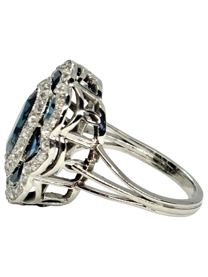 Bague ancienne en or blanc 18K (750 millièmes), sertie d’un saphir naturel central ovale d’environ 2 carats et de petits saphirs naturels en demi-lune. Des diamants naturels de taille ancienne complètent cette pièce de joaillerie pour un poids total d’environ 0,25 carat. Cette bague vintage en or blanc séduit par son élégance intemporelle, ses pierres précieuses et son charme raffiné.