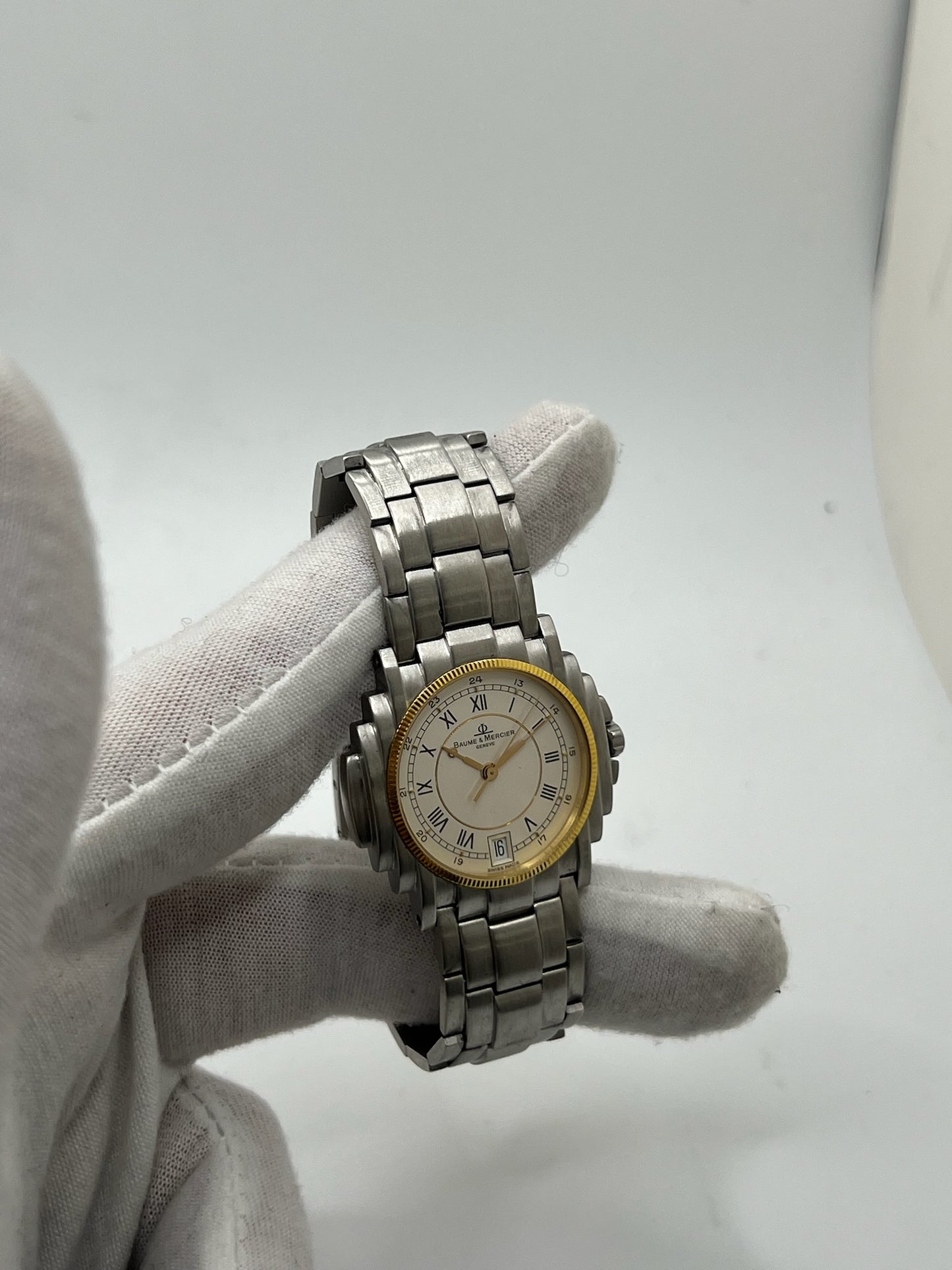 Montre Baume & Mercier 5136.018.3 pour homme/unisexe, boîtier 34 mm en or et acier, cadran blanc à chiffres romains, mouvement quartz précis. Verre saphir résistant aux rayures, bracelet en acier avec boucle double plis. Fonction date. Montre d’occasion en très bon état avec papiers d’origine, élégante et intemporelle.