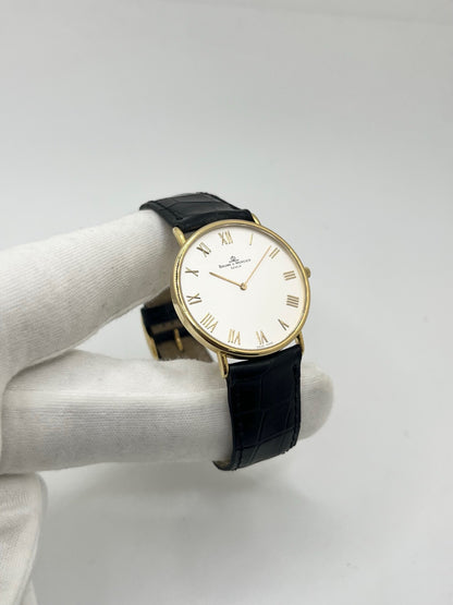Montre Baume & Mercier Classima 15172A en or jaune, équipée d’un mouvement à quartz et d’un boîtier de 33 mm. Son cadran blanc à chiffres romains apporte une allure élégante et intemporelle, tandis que le verre saphir assure sa protection. Ce modèle est monté sur un bracelet noir en cuir de crocodile avec boucle ardillon en acier. Une montre raffinée, idéale pour une tenue chic et élégante, en très bon état.