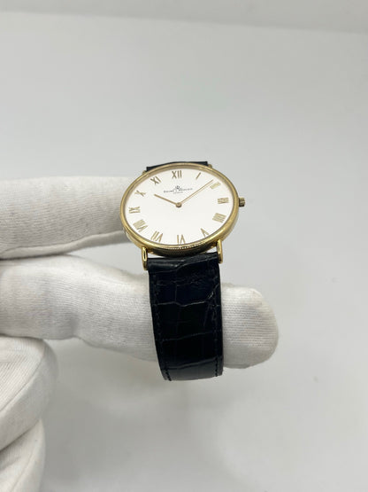 Montre Baume & Mercier Classima 15172A en or jaune, équipée d’un mouvement à quartz et d’un boîtier de 33 mm. Son cadran blanc à chiffres romains apporte une allure élégante et intemporelle, tandis que le verre saphir assure sa protection. Ce modèle est monté sur un bracelet noir en cuir de crocodile avec boucle ardillon en acier. Une montre raffinée, idéale pour une tenue chic et élégante, en très bon état.