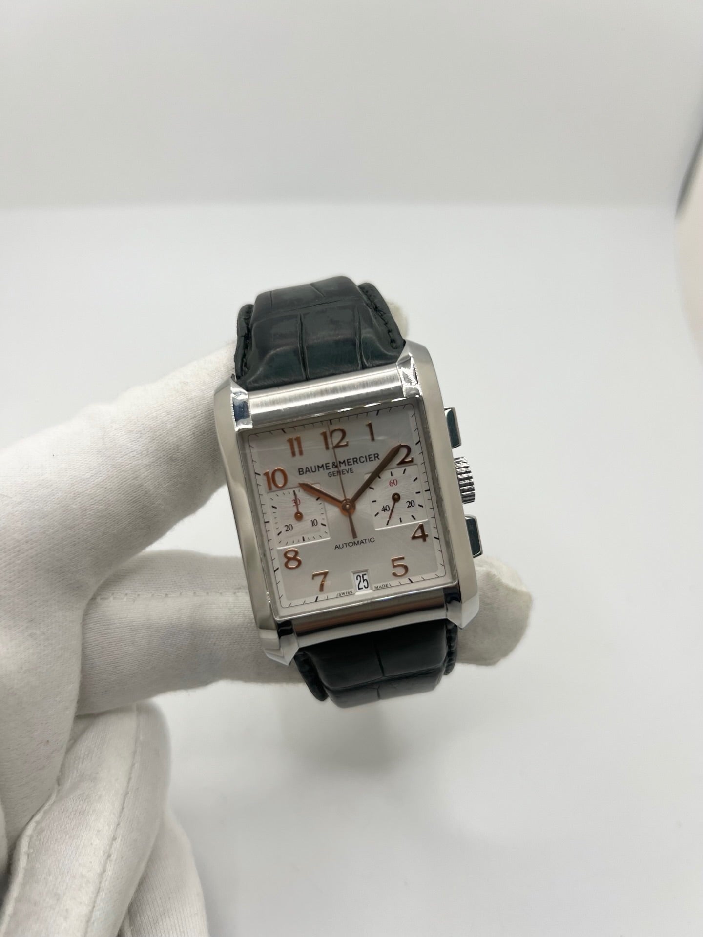 Montre Baume & Mercier Hampton réf. 65698, modèle automatique pour homme ou unisexe. Boîtier en acier de 34,5 mm avec verre saphir résistant aux rayures. Cadran argent avec index en chiffres arabes, offrant une lecture élégante et classique. Bracelet en cuir vert avec boucle déployante en acier. Fonction chronographe et date. Montre de luxe d’occasion en très bon état, avec légères traces d’usure. Révisée le 24 juin 2026 en interne. Livrée sans coffret ni papiers. Disponible à Paris.