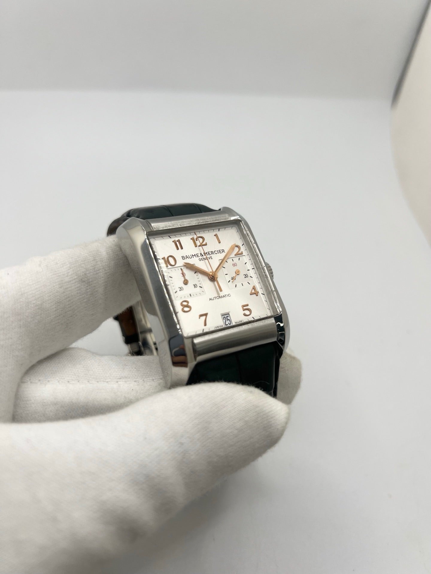 Montre Baume & Mercier Hampton réf. 65698, modèle automatique pour homme ou unisexe. Boîtier en acier de 34,5 mm avec verre saphir résistant aux rayures. Cadran argent avec index en chiffres arabes, offrant une lecture élégante et classique. Bracelet en cuir vert avec boucle déployante en acier. Fonction chronographe et date. Montre de luxe d’occasion en très bon état, avec légères traces d’usure. Révisée le 24 juin 2026 en interne. Livrée sans coffret ni papiers. Disponible à Paris.