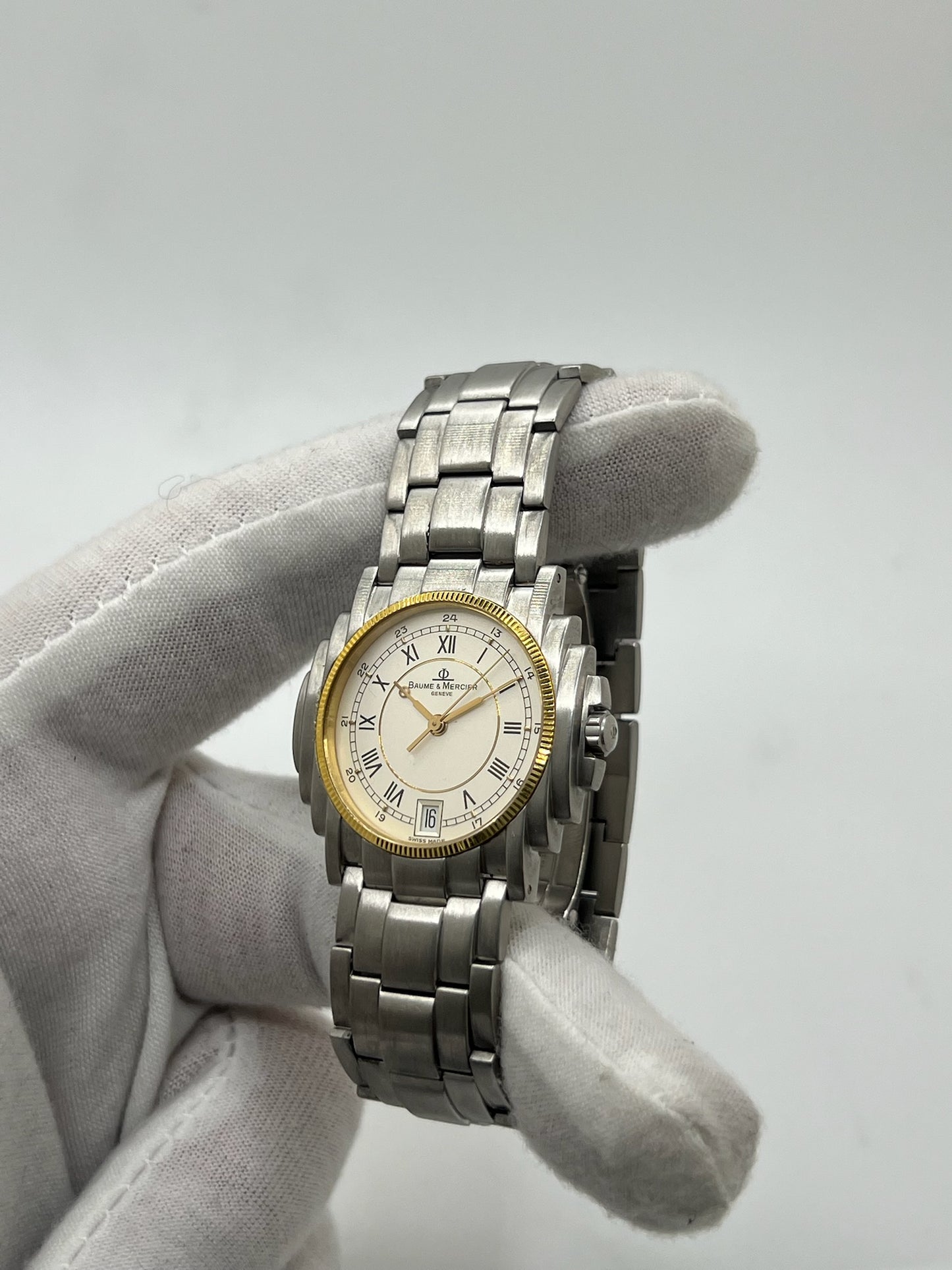 Montre Baume & Mercier 5136.018.3 pour homme/unisexe, boîtier 34 mm en or et acier, cadran blanc à chiffres romains, mouvement quartz précis. Verre saphir résistant aux rayures, bracelet en acier avec boucle double plis. Fonction date. Montre d’occasion en très bon état avec papiers d’origine, élégante et intemporelle.