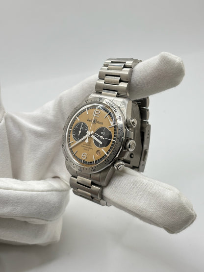 Montre Bell & Ross BR V2 Chronograph Heritage référence BRV2-94-S équipée d'un mouvement automatique. Son boîtier en acier de 41 mm est associé à un bracelet en acier argenté avec boucle déployante double plis. Le cadran doré à chiffres arabes est protégé par un verre minéral et intègre les fonctions chronographe et date. Cette montre d'occasion, révisée en interne et proposée en très bon état, allie esprit aviation, design vintage et précision horlogère suisse.