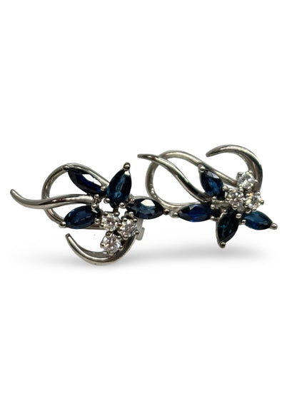 Boucles d’oreilles en or blanc 18K ornées de saphirs totalisant 0,60 ct et de diamants de 0,20 ct. Élégantes et raffinées, elles associent l’intensité bleue des saphirs à l’éclat subtil des diamants. Cette paire intemporelle sublime toutes les tenues et constitue un bijou précieux, idéal pour offrir ou compléter une collection de joaillerie fine.
