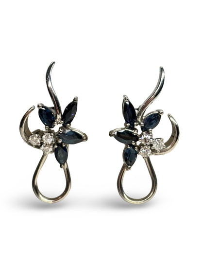 Boucles d’oreilles en or blanc 18K ornées de saphirs totalisant 0,60 ct et de diamants de 0,20 ct. Élégantes et raffinées, elles associent l’intensité bleue des saphirs à l’éclat subtil des diamants. Cette paire intemporelle sublime toutes les tenues et constitue un bijou précieux, idéal pour offrir ou compléter une collection de joaillerie fine.
