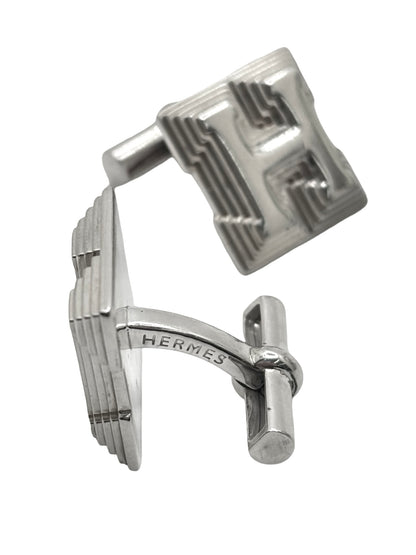 Boutons de manchettes Hermès en argent 925 au style élégant et intemporel. Cette paire raffinée en argent massif séduit par ses finitions soignées et son design sophistiqué caractéristique du savoir-faire Hermès. Accessoires de luxe parfaits pour compléter un costume, une tenue habillée ou une cérémonie. Boutons de manchettes précieux alliant distinction, élégance masculine et qualité joaillière dans un esprit chic et contemporain.
