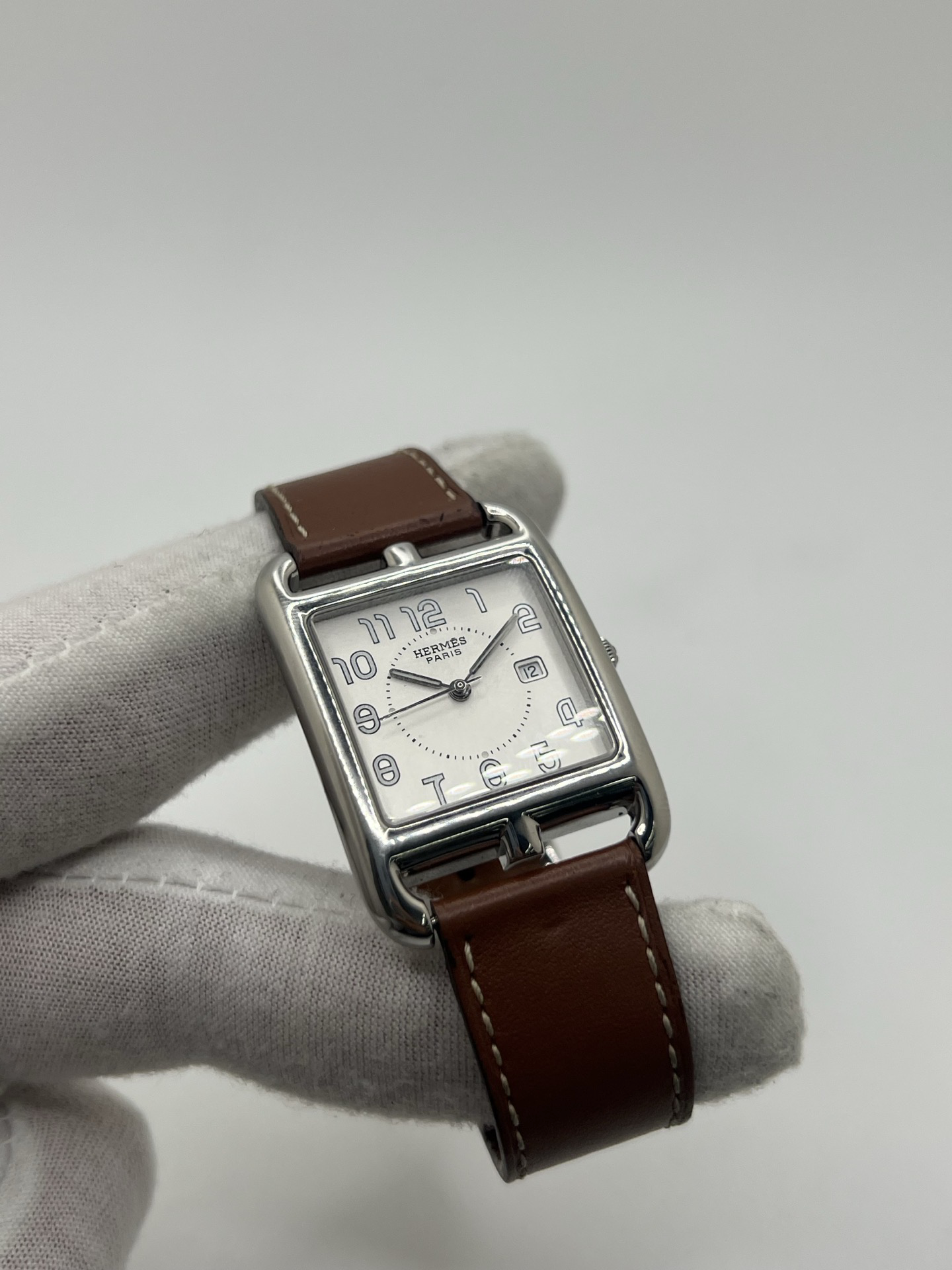 Montre Hermès Cape Cod Grand Modèle en acier inoxydable, boîtier rectangulaire iconique aux lignes élégantes et contemporaines, cadran argenté épuré avec chiffres arabes stylisés et aiguilles fines. Bracelet en cuir signature Hermès offrant confort et raffinement. Mouvement quartz précis. Montre de luxe intemporelle et sophistiquée, idéale pour un porté quotidien ou une tenue habillée, symbole du savoir-faire horloger et du style parisien.