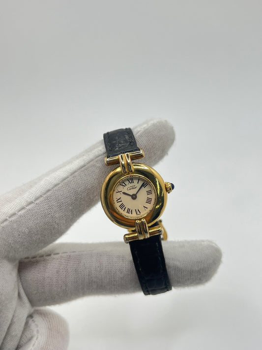 Montre Cartier Colisée Must Vermeil réf. 590002 pour femme, équipée d’un mouvement quartz précis. Boîtier en argent vermeil de 24 mm, cadran blanc à chiffres romains, verre saphir et bracelet en cuir noir avec boucle ardillon. Modèle d’occasion en bon état présentant quelques traces d’usure. Idéal pour les amateurs de montres élégantes et intemporelles.