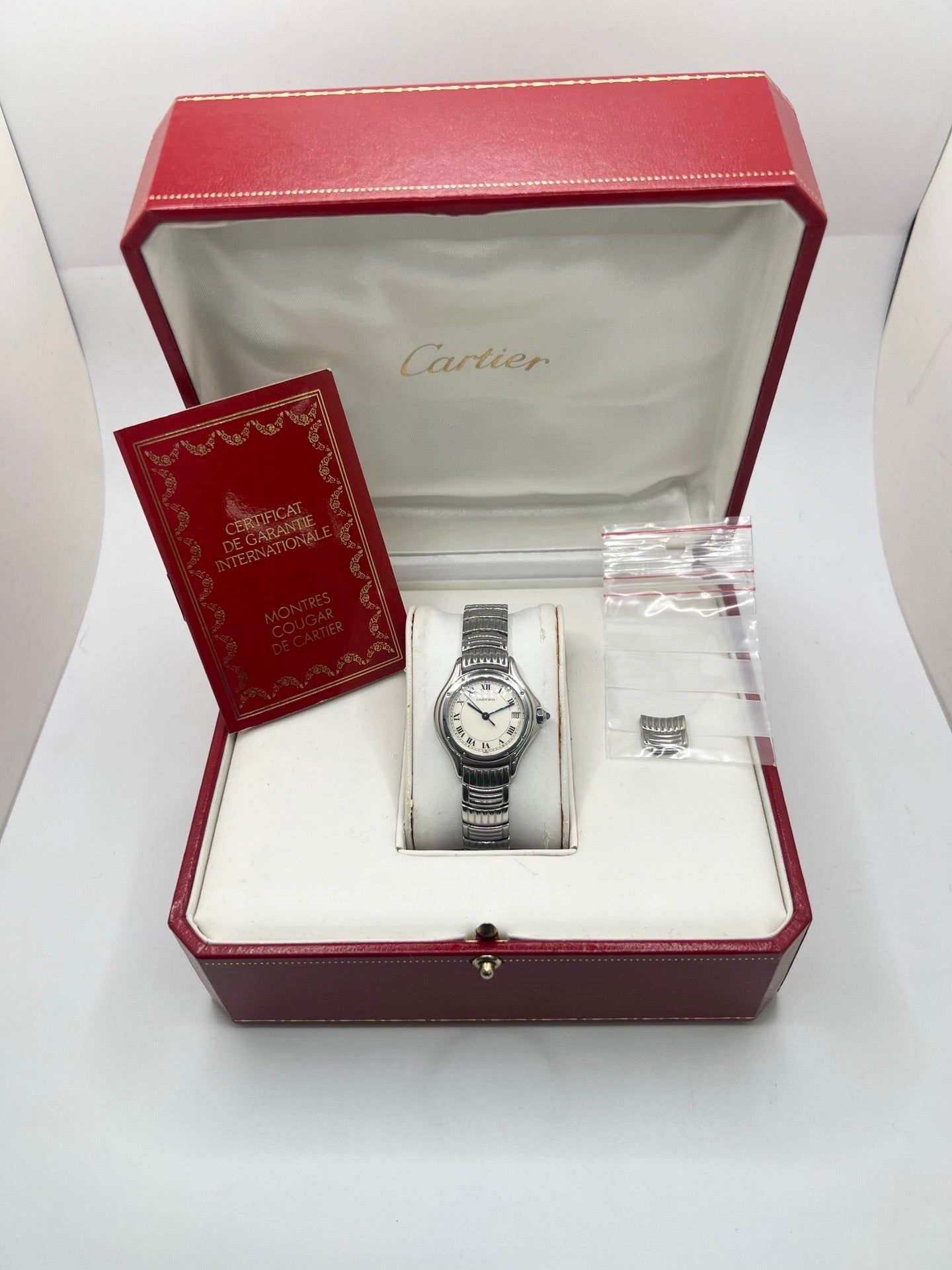 Montre Cartier Cougar référence 1215 1 en acier inoxydable avec boîtier de 26 mm et bracelet assorti. Ce modèle à mouvement quartz se distingue par son cadran blanc à chiffres romains, son verre saphir résistant aux rayures et son affichage de la date. Son design emblématique allie élégance et sobriété, caractéristique des créations horlogères de la maison Cartier. Montre d'occasion de 1995 en très bon état, révisée, avec coffret et papiers d'origine.
