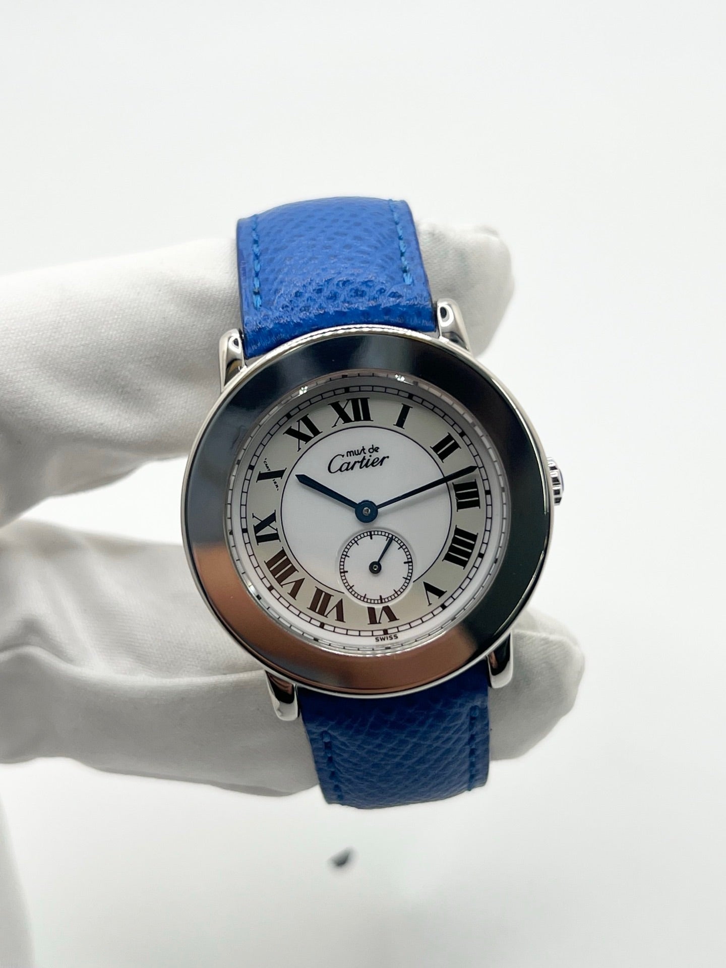 Montre Cartier Must de Cartier Ronde, modèle femme élégant à mouvement quartz. Boîtier rond en métal précieux, cadran blanc raffiné avec chiffres romains, design classique signature Cartier. Bracelet cuir bleu avec boucle ardillon en acier. Verre saphir résistant, diamètre 33 mm. Montre de luxe d’occasion en très bon état, avec légères traces d’usage peu visibles. Révisée en interne le 22 avril 2026. Livrée avec coffret d’origine, sans papiers, disponible à Paris.
