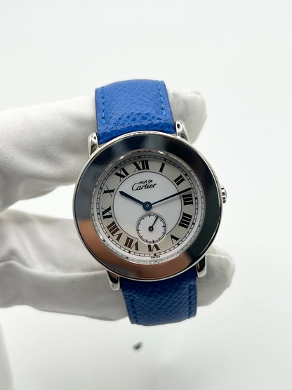 Montre Cartier Must de Cartier Ronde, modèle femme élégant à mouvement quartz. Boîtier rond en métal précieux, cadran blanc raffiné avec chiffres romains, design classique signature Cartier. Bracelet cuir bleu avec boucle ardillon en acier. Verre saphir résistant, diamètre 33 mm. Montre de luxe d’occasion en très bon état, avec légères traces d’usage peu visibles. Révisée en interne le 22 avril 2026. Livrée avec coffret d’origine, sans papiers, disponible à Paris.
