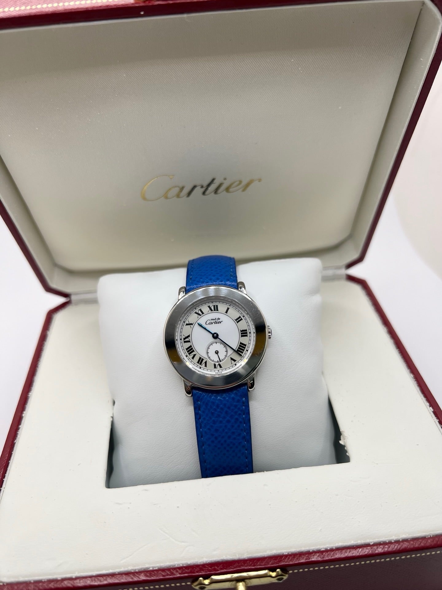 Montre Cartier Must de Cartier Ronde, modèle femme élégant à mouvement quartz. Boîtier rond en métal précieux, cadran blanc raffiné avec chiffres romains, design classique signature Cartier. Bracelet cuir bleu avec boucle ardillon en acier. Verre saphir résistant, diamètre 33 mm. Montre de luxe d’occasion en très bon état, avec légères traces d’usage peu visibles. Révisée en interne le 22 avril 2026. Livrée avec coffret d’origine, sans papiers, disponible à Paris.
