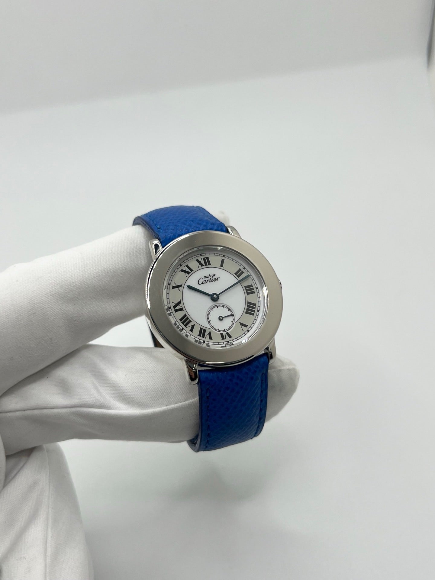Montre Cartier Must de Cartier Ronde, modèle femme élégant à mouvement quartz. Boîtier rond en métal précieux, cadran blanc raffiné avec chiffres romains, design classique signature Cartier. Bracelet cuir bleu avec boucle ardillon en acier. Verre saphir résistant, diamètre 33 mm. Montre de luxe d’occasion en très bon état, avec légères traces d’usage peu visibles. Révisée en interne le 22 avril 2026. Livrée avec coffret d’origine, sans papiers, disponible à Paris.

