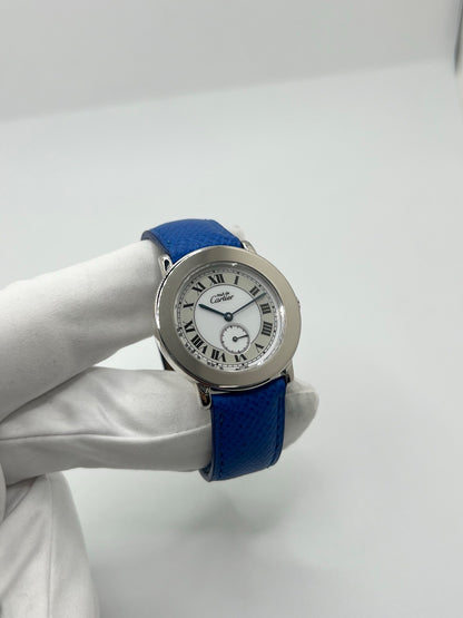 Montre Cartier Must de Cartier Ronde, modèle femme élégant à mouvement quartz. Boîtier rond en métal précieux, cadran blanc raffiné avec chiffres romains, design classique signature Cartier. Bracelet cuir bleu avec boucle ardillon en acier. Verre saphir résistant, diamètre 33 mm. Montre de luxe d’occasion en très bon état, avec légères traces d’usage peu visibles. Révisée en interne le 22 avril 2026. Livrée avec coffret d’origine, sans papiers, disponible à Paris.
