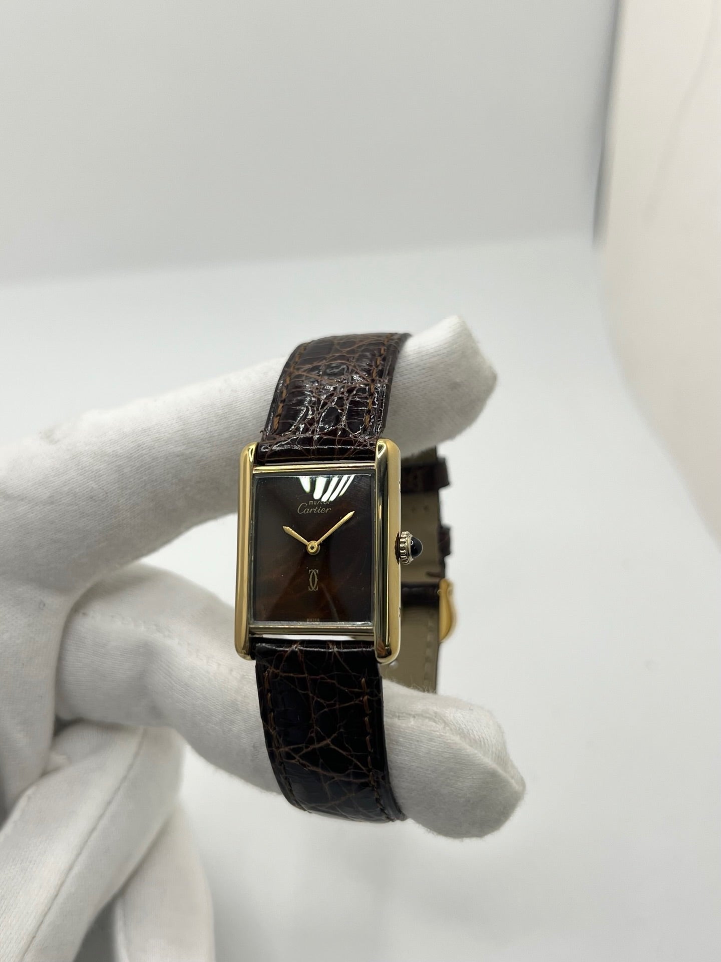 Montre Cartier Tank Must Vermeil Œil de Tigre vintage avec boîtier rectangulaire en vermeil, mouvement à remontage manuel et cadran en pierre naturelle œil de tigre aux reflets bruns et dorés. Cette Cartier Must Tank Vermeil se distingue par son design emblématique, son bracelet en cuir brun et son élégance intemporelle. Montre de collection recherchée par les amateurs de montres Cartier vintage, alliant raffinement, caractère et savoir-faire horloger.