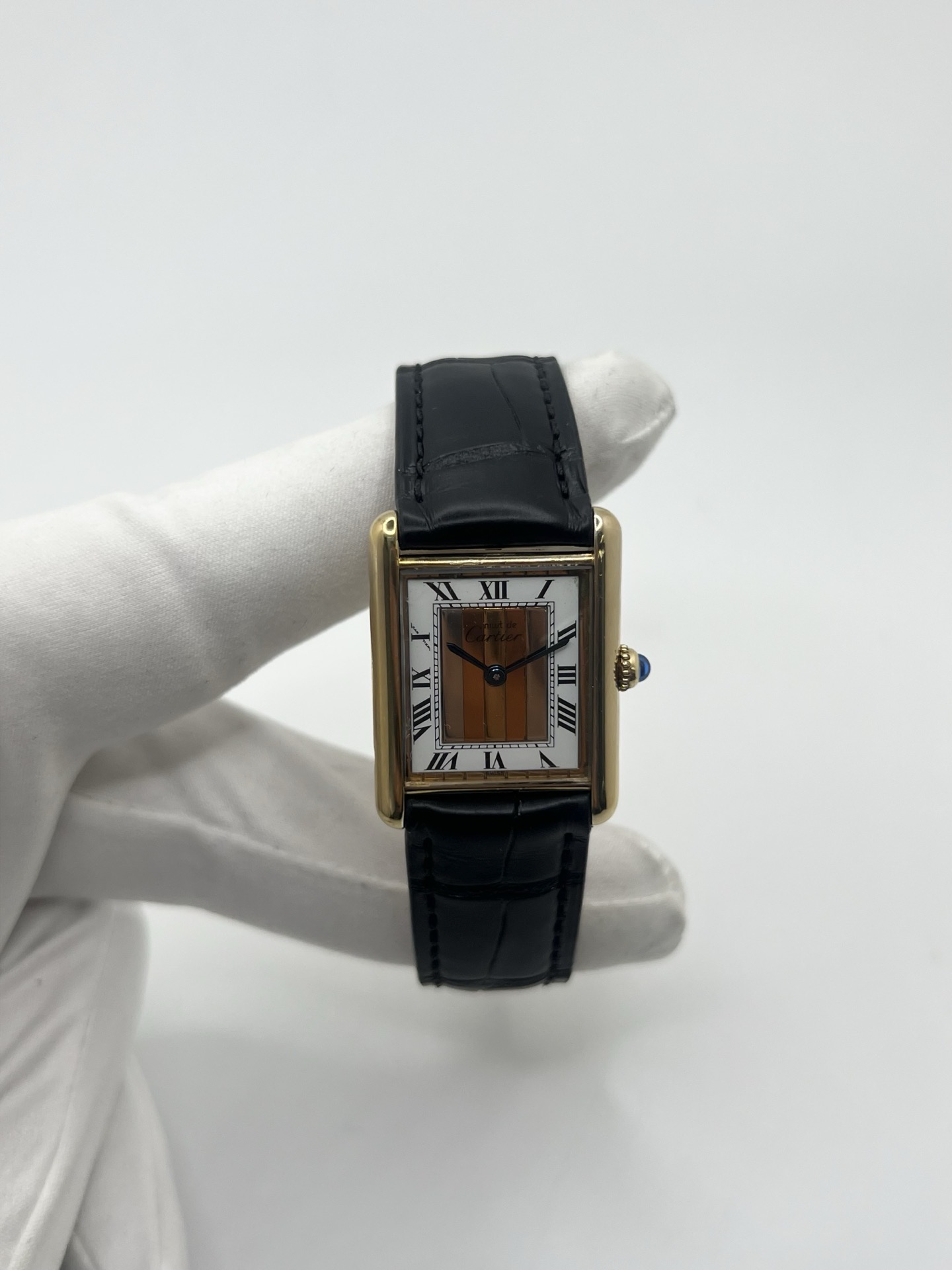 Montre Cartier Tank Must Trinity Grand Modèle vintage en vermeil, référence 590005, datant des années 1990. Boîtier rectangulaire de 23 x 30 mm en argent vermeil, cadran blanc à chiffres romains avec motif Trinity emblématique, verre saphir et mouvement quartz Cartier calibre 90. Bracelet en cuir avec boucle Cartier. Cette montre de luxe au design intemporel incarne l’élégance française et l’héritage horloger de Cartier, recherchée par les collectionneurs de montres vintage.
