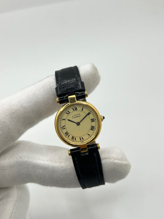 Montre Cartier Must Vendôme en vermeil, boîtier en argent plaqué or au diamètre de 30 mm, accompagnée d’un cadran blanc à chiffres romains signature. Équipée d’un mouvement quartz précis et d’un bracelet en cuir noir avec boucle en acier. Modèle élégant et intemporel, idéal pour un poignet féminin. Montre d’occasion en très bon état, présentant de légères micro-rayures, révisée en interne, livrée avec son coffret d’origine.