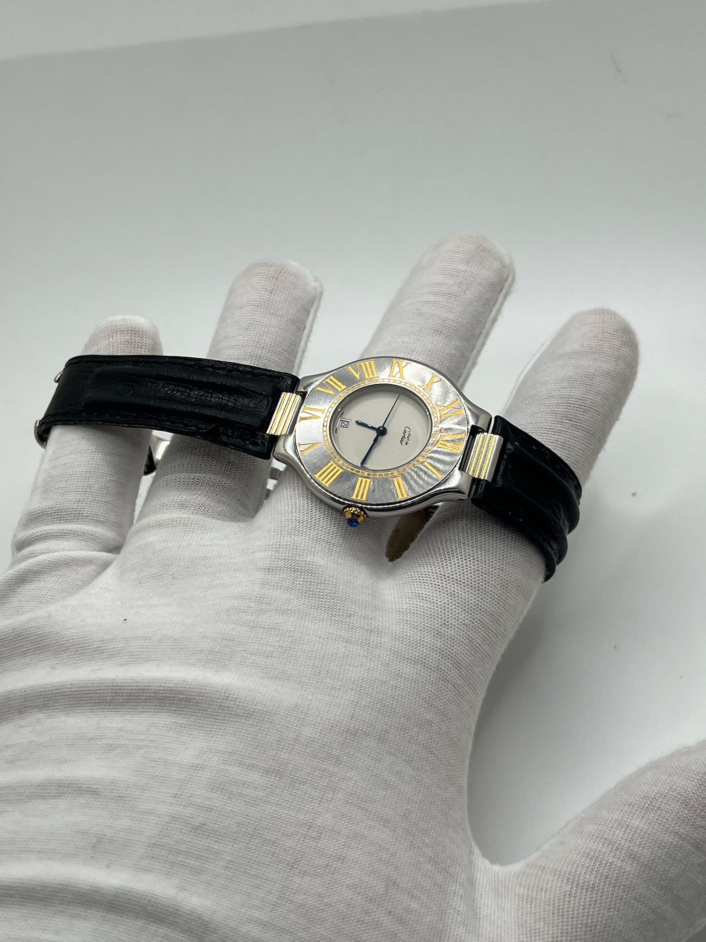 Montre Cartier 21 Must de Cartier avec boîtier 35 mm en or et acier, cadran blanc à chiffres romains, mouvement quartz. Modèle élégant et mixte, équipé d’une boucle déployante sur bracelet cuir noir. Montre de luxe vintage en très bon état, révisée, disponible sans boîte ni papiers d’origine. Idéale pour collectionneur ou amateur de montres emblématiques signées Cartier.