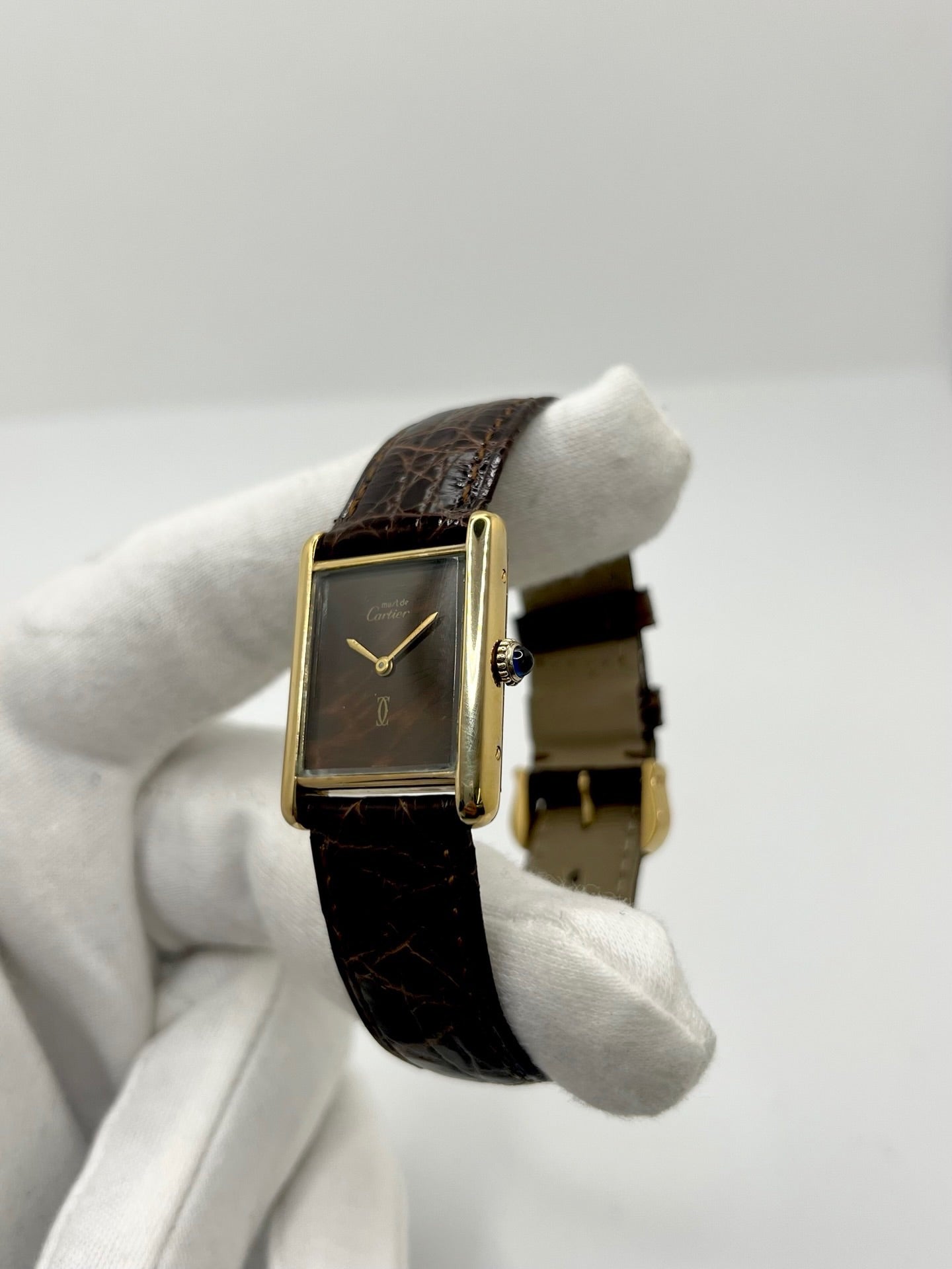 Montre Cartier Tank Must Vermeil Œil de Tigre vintage avec boîtier rectangulaire en vermeil, mouvement à remontage manuel et cadran en pierre naturelle œil de tigre aux reflets bruns et dorés. Cette Cartier Must Tank Vermeil se distingue par son design emblématique, son bracelet en cuir brun et son élégance intemporelle. Montre de collection recherchée par les amateurs de montres Cartier vintage, alliant raffinement, caractère et savoir-faire horloger.