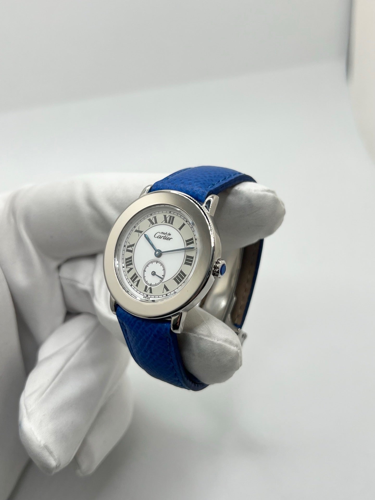 Montre Cartier Must de Cartier Ronde, modèle femme élégant à mouvement quartz. Boîtier rond en métal précieux, cadran blanc raffiné avec chiffres romains, design classique signature Cartier. Bracelet cuir bleu avec boucle ardillon en acier. Verre saphir résistant, diamètre 33 mm. Montre de luxe d’occasion en très bon état, avec légères traces d’usage peu visibles. Révisée en interne le 22 avril 2026. Livrée avec coffret d’origine, sans papiers, disponible à Paris.
