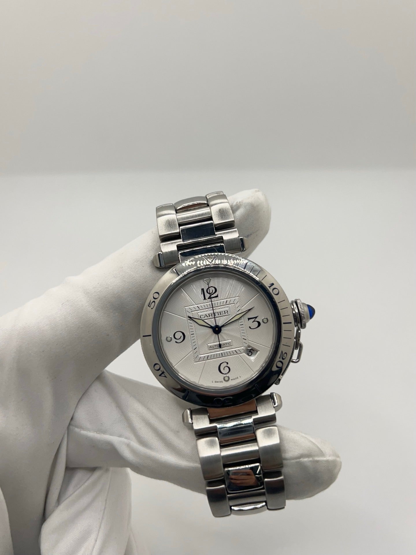 Montre Cartier Pasha automatique en acier, boîtier 38 mm avec verre saphir et cadran argent à chiffres arabes. Équipée d’un mouvement automatique calibre Cartier 191 avec fonction date. Bracelet acier avec boucle déployante. Modèle d’occasion en très bon état, révisé, présentant de légères micro-rayures peu visibles. Montre élégante et sportive, adaptée à un usage quotidien, livrée avec son coffret d’origine.
