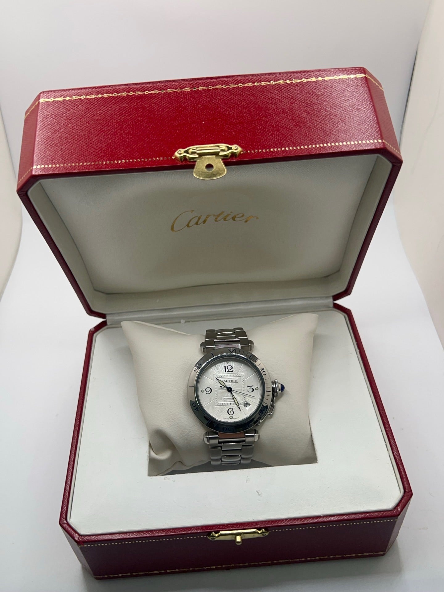 Montre Cartier Pasha automatique en acier, boîtier 38 mm avec verre saphir et cadran argent à chiffres arabes. Équipée d’un mouvement automatique calibre Cartier 191 avec fonction date. Bracelet acier avec boucle déployante. Modèle d’occasion en très bon état, révisé, présentant de légères micro-rayures peu visibles. Montre élégante et sportive, adaptée à un usage quotidien, livrée avec son coffret d’origine.

