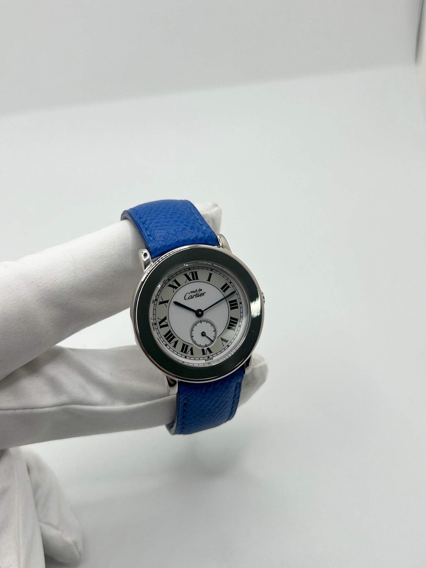 Montre Cartier Must de Cartier Ronde, modèle femme élégant à mouvement quartz. Boîtier rond en métal précieux, cadran blanc raffiné avec chiffres romains, design classique signature Cartier. Bracelet cuir bleu avec boucle ardillon en acier. Verre saphir résistant, diamètre 33 mm. Montre de luxe d’occasion en très bon état, avec légères traces d’usage peu visibles. Révisée en interne le 22 avril 2026. Livrée avec coffret d’origine, sans papiers, disponible à Paris.
