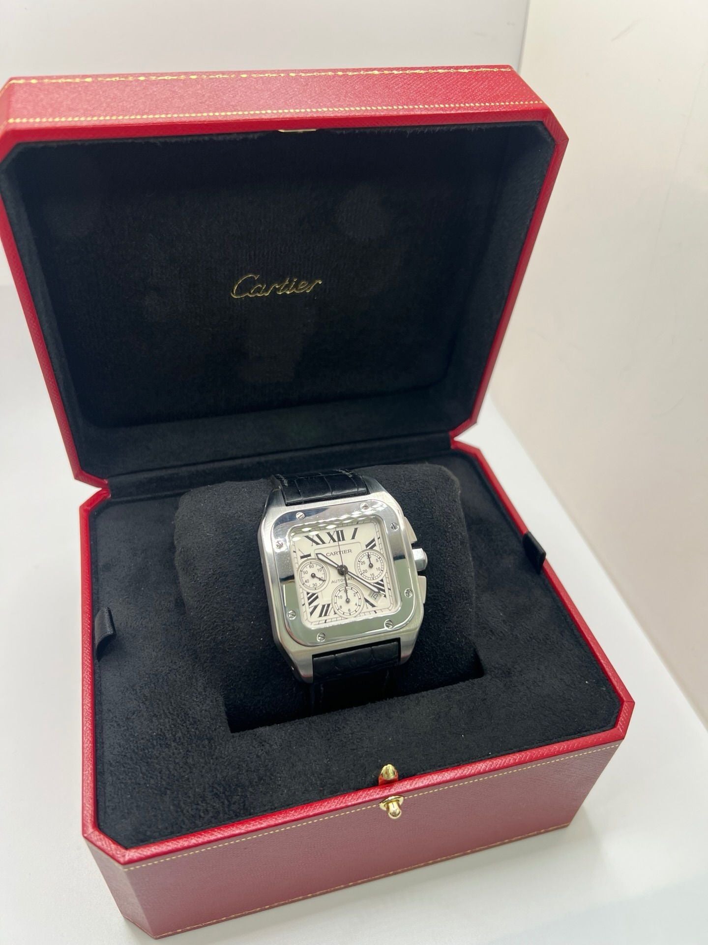 Montre Cartier Santos 100 XL Chronograph pour homme, modèle emblématique au design sport-chic. Boîtier en acier, cadran blanc à chiffres romains, bracelet en cuir noir. Mouvement automatique précis avec chronographe et date. Montre d’occasion en excellent état, révisée, livrée avec coffret d’origine.
