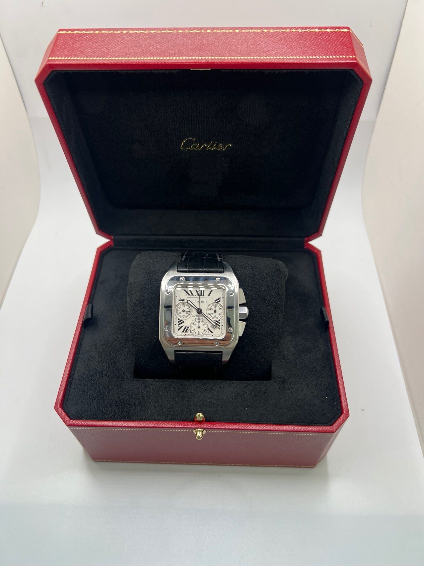 Montre Cartier Santos 100 XL Chronograph pour homme, modèle emblématique au design sport-chic. Boîtier en acier, cadran blanc à chiffres romains, bracelet en cuir noir. Mouvement automatique précis avec chronographe et date. Montre d’occasion en excellent état, révisée, livrée avec coffret d’origine.