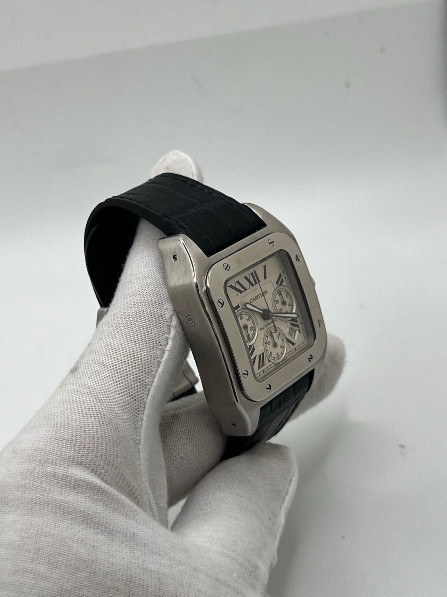 Montre Cartier Santos 100 XL Chronograph pour homme, modèle emblématique au design sport-chic. Boîtier en acier, cadran blanc à chiffres romains, bracelet en cuir noir. Mouvement automatique précis avec chronographe et date. Montre d’occasion en excellent état, révisée, livrée avec coffret d’origine.