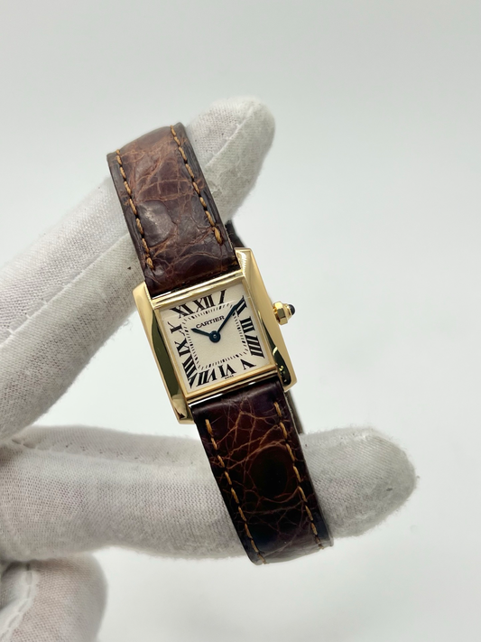 Montre Cartier Tank Française référence 1820 en or jaune 18K, petit modèle pour femme, boîtier rectangulaire emblématique aux lignes droites et élégantes, cadran blanc avec chiffres romains noirs, minuterie chemin de fer et aiguilles bleuies en forme de glaive. Bracelet intégré en acier avec boucle déployante. Mouvement quartz précis. Montre de luxe intemporelle, raffinée et iconique, idéale pour un porté quotidien ou une tenue habillée.
