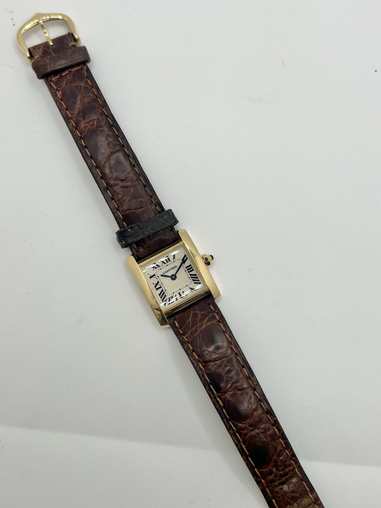Montre Cartier Tank Française référence 1820 en or jaune 18K, petit modèle pour femme, boîtier rectangulaire emblématique aux lignes droites et élégantes, cadran blanc avec chiffres romains noirs, minuterie chemin de fer et aiguilles bleuies en forme de glaive. Bracelet intégré en acier avec boucle déployante. Mouvement quartz précis. Montre de luxe intemporelle, raffinée et iconique, idéale pour un porté quotidien ou une tenue habillée.