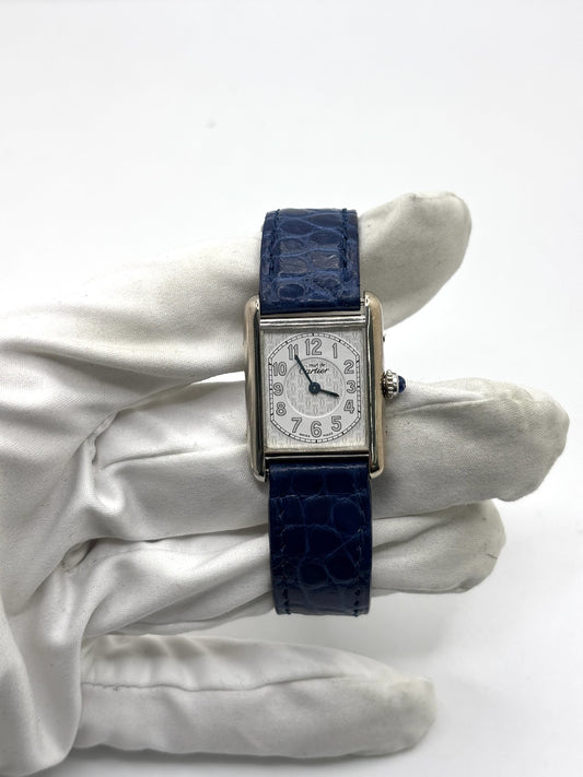 Montre Cartier Tank Must référence 2416 en argent avec cadran blanc à chiffres arabes et mouvement quartz. Ce modèle iconique présente un boîtier rectangulaire de 22 x 30 mm, une lunette en argent et un bracelet en cuir bleu avec boucle ardillon en acier. Cartier Tank Must d'occasion en très bon état, avec de légères traces d'usure. Montre homme ou unisexe élégante et intemporelle, idéale pour les amateurs d'horlogerie et de montres de luxe vintage.
