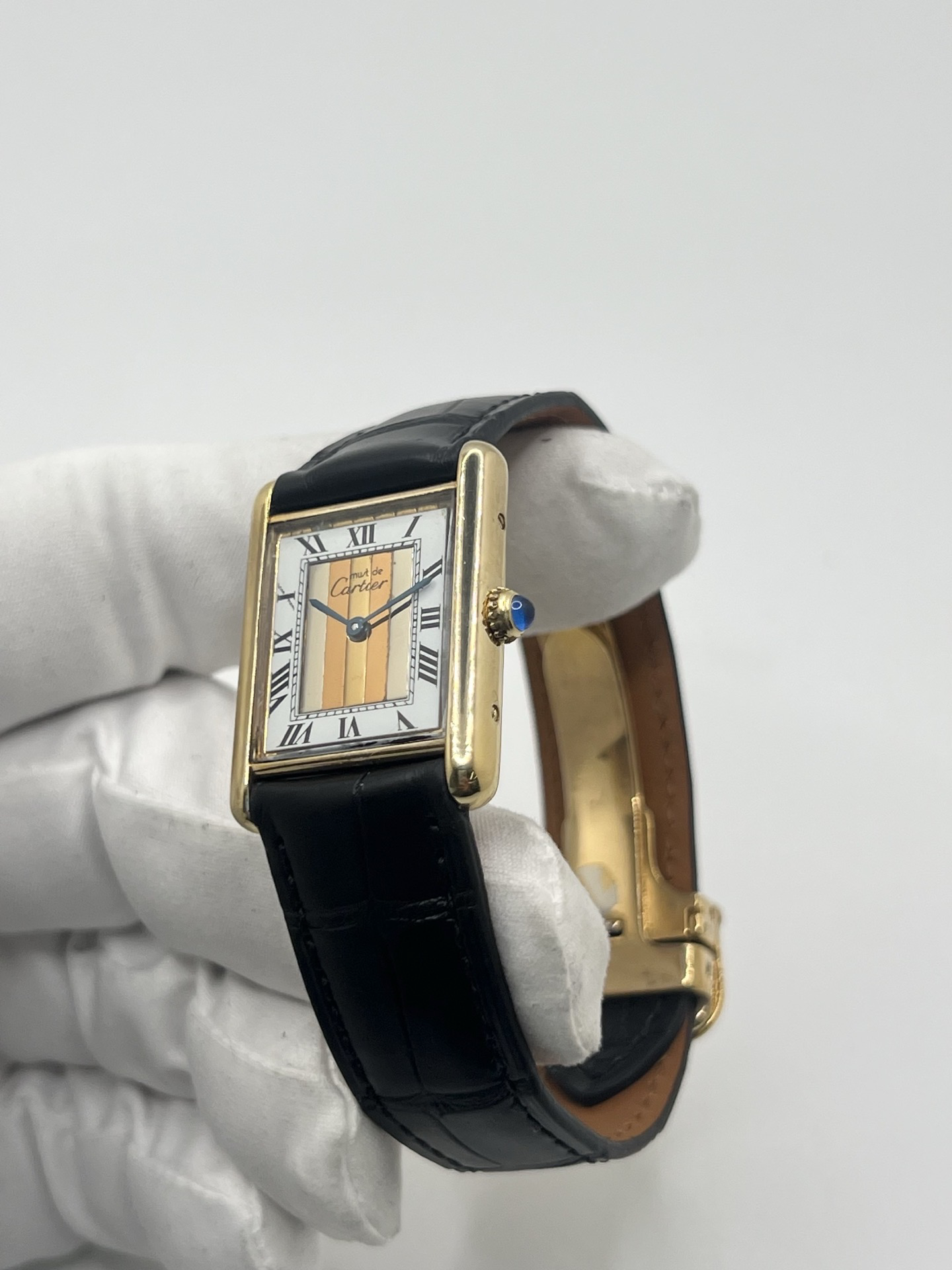 Montre Cartier Tank Must Trinity Grand Modèle vintage en vermeil, référence 590005, datant des années 1990. Boîtier rectangulaire de 23 x 30 mm en argent vermeil, cadran blanc à chiffres romains avec motif Trinity emblématique, verre saphir et mouvement quartz Cartier calibre 90. Bracelet en cuir avec boucle Cartier. Cette montre de luxe au design intemporel incarne l’élégance française et l’héritage horloger de Cartier, recherchée par les collectionneurs de montres vintage.