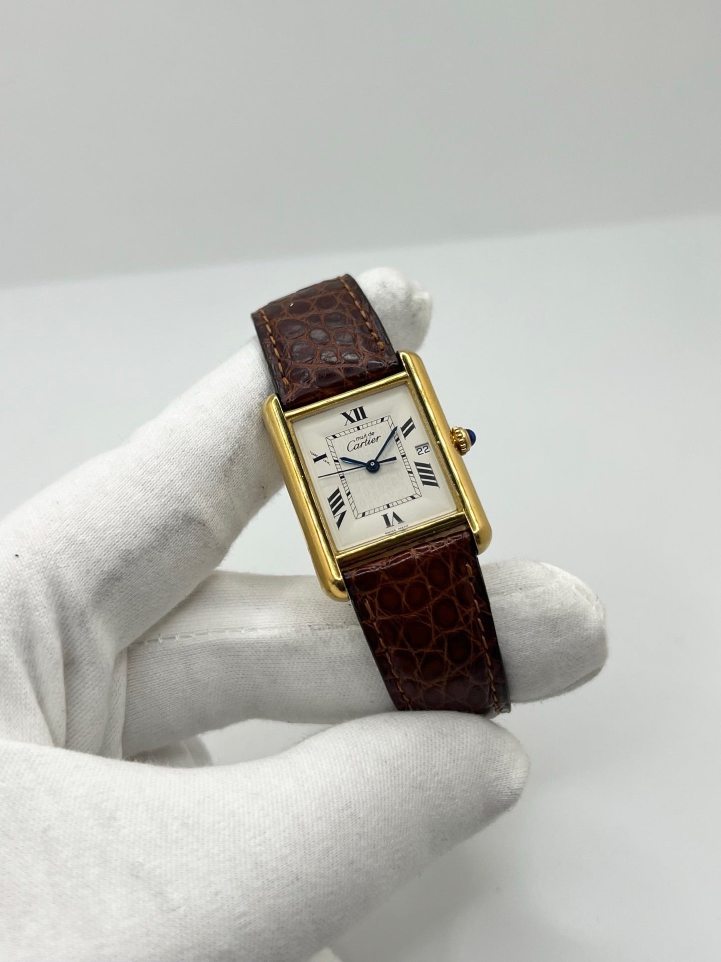 Montre Cartier Tank Must grand modèle en argent avec cadran blanc à chiffres romains, mouvement quartz et fonction date. Boîtier rectangulaire 25 x 33 mm avec verre minéral, bracelet en cuir brun et boucle ardillon en acier. Modèle iconique au design élégant et intemporel, idéal pour homme ou unisexe. Montre d’occasion en bon état, révisée, avec coffret d’origine.