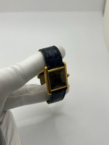 Montre Cartier Must de Cartier Tank Trinity en argent, à remontage manuel, avec boîtier de 23 x 30 mm et cadran jaune sans chiffres. Ce modèle emblématique est équipé d’un bracelet en cuir bleu avec boucle ardillon en acier, d’un verre minéral et d’une lunette en argent. Montre de luxe vintage homme ou unisexe, d’occasion en bon état, présentant des traces d’usure visibles. Révisée en interne, livrée avec coffret d’origine, idéale pour les collectionneurs de montres Cartier Tank Trinity.