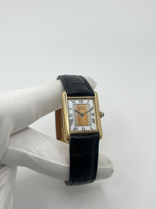 Montre Cartier Tank Must Trinity Grand Modèle vintage en vermeil, référence 590005, datant des années 1990. Boîtier rectangulaire de 23 x 30 mm en argent vermeil, cadran blanc à chiffres romains avec motif Trinity emblématique, verre saphir et mouvement quartz Cartier calibre 90. Bracelet en cuir avec boucle Cartier. Cette montre de luxe au design intemporel incarne l’élégance française et l’héritage horloger de Cartier, recherchée par les collectionneurs de montres vintage.