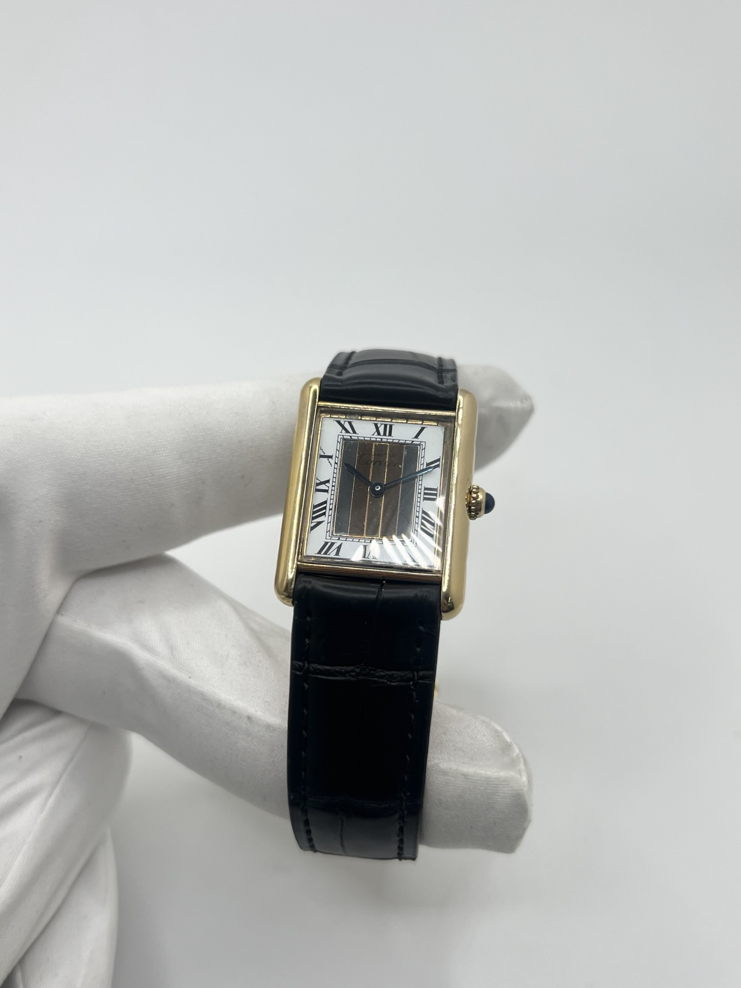 Montre Cartier Tank Must Trinity Grand Modèle vintage en vermeil, référence 590005, datant des années 1990. Boîtier rectangulaire de 23 x 30 mm en argent vermeil, cadran blanc à chiffres romains avec motif Trinity emblématique, verre saphir et mouvement quartz Cartier calibre 90. Bracelet en cuir avec boucle Cartier. Cette montre de luxe au design intemporel incarne l’élégance française et l’héritage horloger de Cartier, recherchée par les collectionneurs de montres vintage.