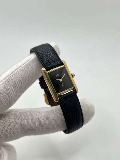 Montre Cartier Tank Must Vermeil référence 5057001 pour femme, boîtier en argent 20 x 28 mm, cadran noir sans chiffres et bracelet en cuir de lézard noir. Modèle à mouvement quartz, en bon état avec traces d’usure légères. Montre élégante au style intemporel, idéale pour un look sophistiqué et raffiné. Parfaite pour les amateurs de pièces vintage.