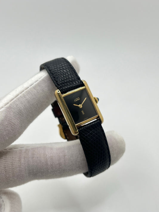 Montre Cartier Tank Must Vermeil référence 5057001 pour femme, boîtier en argent 20 x 28 mm, cadran noir sans chiffres et bracelet en cuir de lézard noir. Modèle à mouvement quartz, en bon état avec traces d’usure légères. Montre élégante au style intemporel, idéale pour un look sophistiqué et raffiné. Parfaite pour les amateurs de pièces vintage.